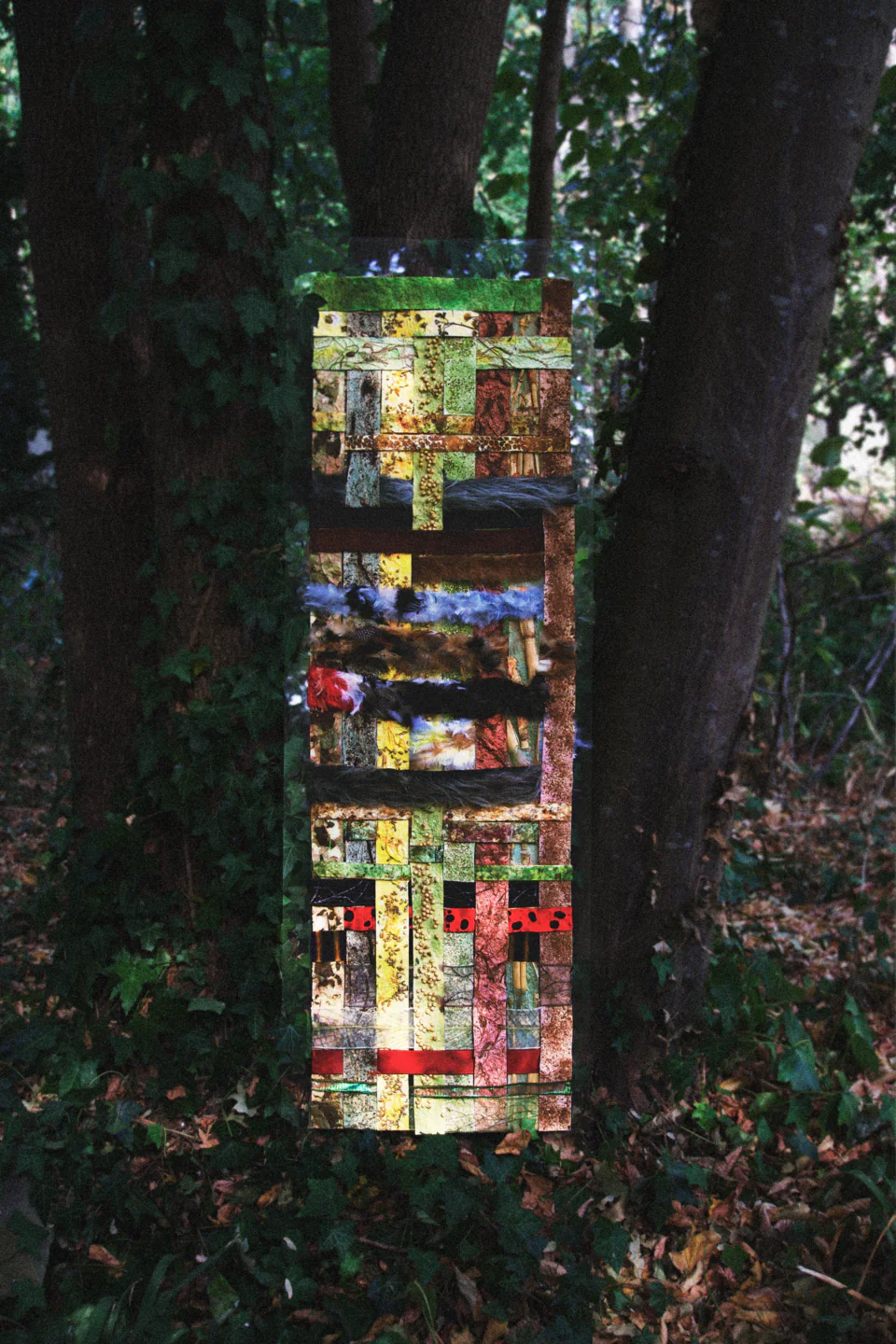 The five-foot Fabric of Life installation hanging on a clear panel between two trees, woven from strips of leaf paper, mycelium leather, feathers and fur